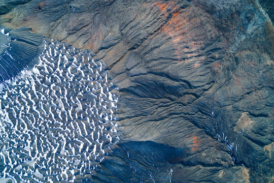 Snow covered hollow on grey eroded slag heap surface with rocky ridges, top view aerial shot