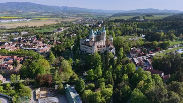 Majestic aerial view of Bojnice Castle, Slovakia, its romantic medieval towers rising above lush parkland and a charming town, creating a fairy tale landscape