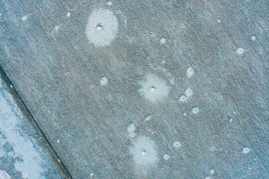 Artillery craters and shell blast sites on snow covered agricultural field in war zone, top view aerial shot