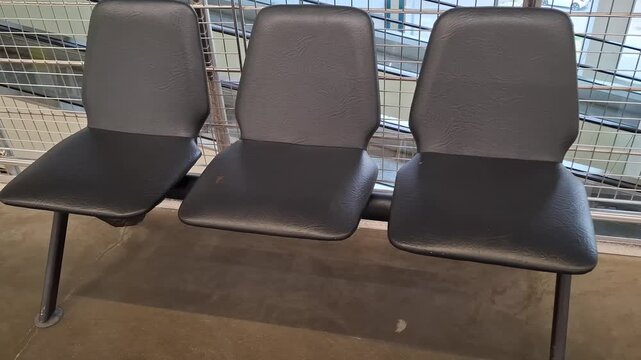 Three empty black plastic chairs stand indoors on a concrete floor in a hypermarket waiting area, large grocery retail supermarket interior, commercial facility furniture.