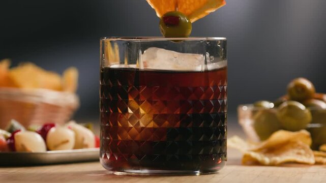 Vermouth, Spanish red, served close-up in a glass with traditional gilda tapas skewer of olives and anchovy on a wooden bar table in a cozy restaurant.