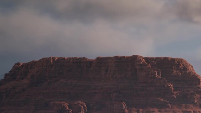 In the early evening, the sun casts shadows on red rock formations at the Grand Canyon. Clouds gather above, adding texture to the scene and creating a dramatic atmosphere.