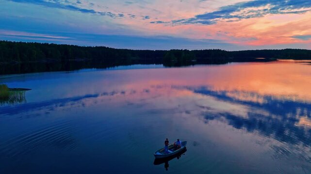 Panoramic drone footage of boat with two anglers on calm reflective lake Matildanjarvi at dusk