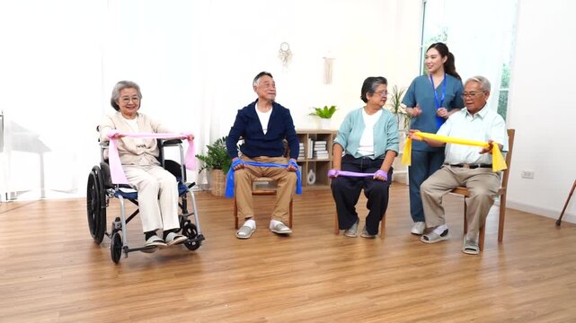 An Asian nurse handed out ribbons containing exercise equipment to a group of elderly people, including some in wheelchairs, in a class at a nursing home
