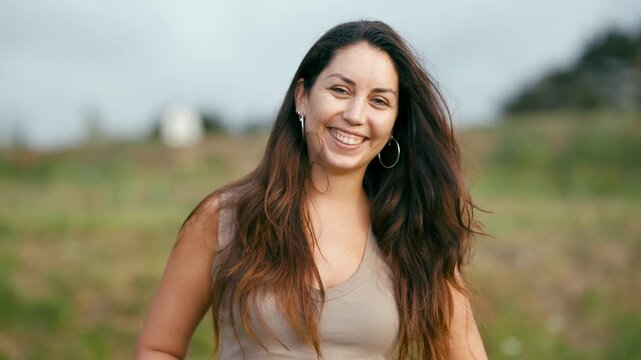Authentic portrait of a pretty young hispanic woman with long hair looking at the camera and laughing. Genuine emotion and happiness