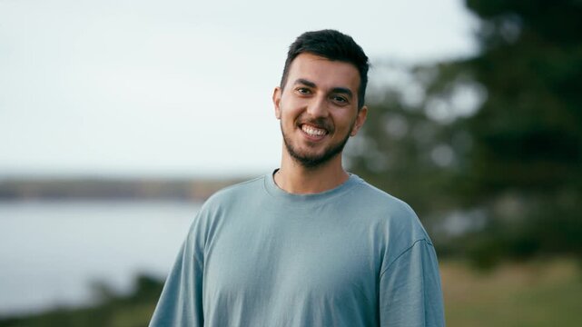 Portrait of a handsome young man standing outdoors. Confident and carefree person smiling and looking at the camera in a natural park setting