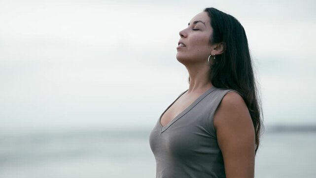 Young serene woman breathing deeply while standing by the ocean. Beautiful pensive lady feeling calm and relaxed, enjoying her freedom
