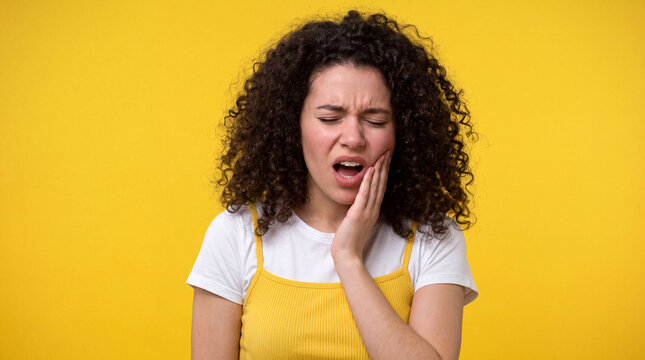 Young Woman Suffering from Severe Toothache Touching Her Cheek on Yellow Background
