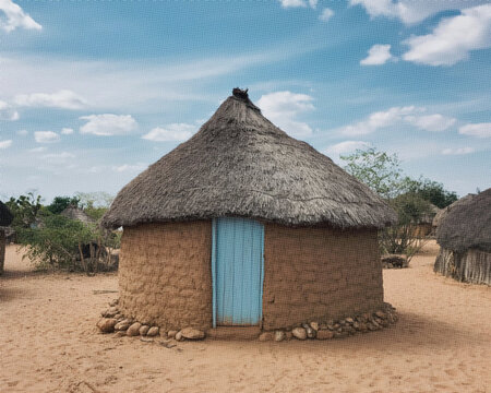 Traditional round hut with a thatched roof and a light blue wooden door in a sandy village area