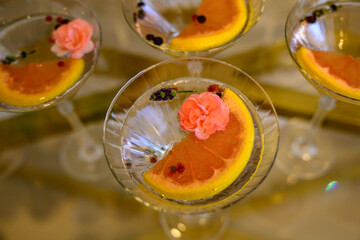These elegant martini glasses are part of a display featuring cocktails garnished with vibrant pink edible flowers and citrus slices. © nedomacki