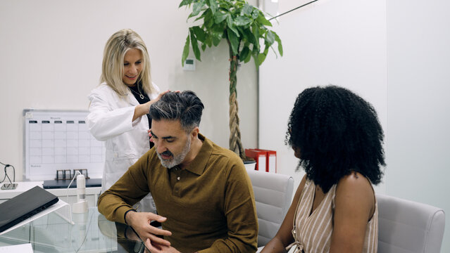 Medical professional consulting male patient about hair loss and scalp health. Consulting partner observes