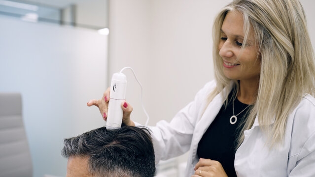 Trichology specialist examining male patient's scalp using a dermatoscope for hair loss and follicle health analysis