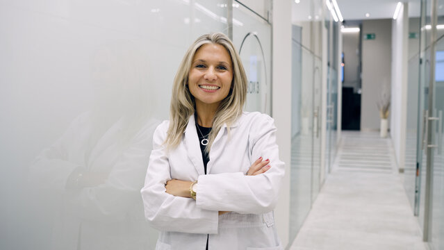 Experienced female doctor wearing a lab coat, arms crossed, smiling. Healthcare professional offering hair treatment services