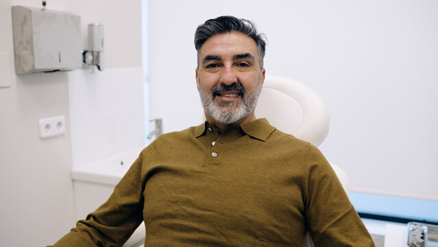 Smiling mature man sitting in a clinic chair, waiting to receive a hair treatment. He is looking at the camera