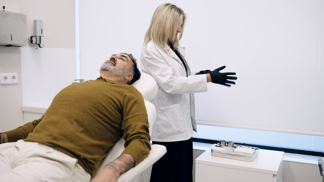 Doctor wearing gloves, preparing for a hair loss treatment procedure for a male client in a modern clinic