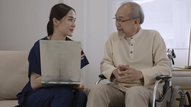 Professional young Asian woman nurse caregiver holding clipboard is talking, explaining, and providing healthcare advice to senior male patient while sitting in wheelchair in special room at hospital.