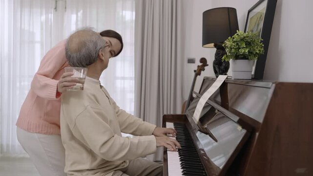 Happy Asian senior elderly father and his beautiful daughter sit playing piano and singing together having fun and enjoying in living room at home. Lifestyle and leisure after retirement with family. 