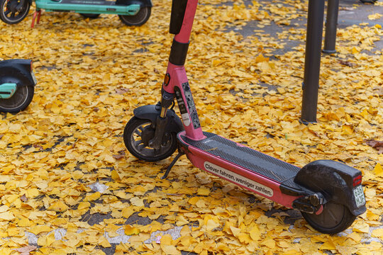 Dusseldorf, Germany - November 19 2025: Rental e-scooter stand among fallen autumn leaves on a city street in central D&uuml;sseldorf, Germany