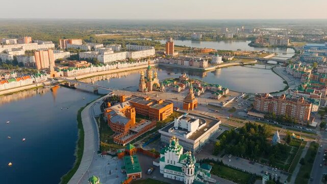 Yoshkar-Ola, Russia. Bruges Embankment along the Malaya Kokshaga River, Flemish-style facades and golden-domed cathedrals, aerial panoramic view at sunset. Drone footage