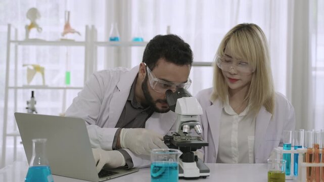 Two professional scientists and researchers are excited and happy about their success in conducting chemistry experiments on a medical vaccine, using a microscope and laptop in the science laboratory.