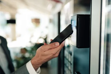 Fotobehang Onderzeeër Man's hand holding a smartphone for an nfc payment or mobile scan at an automated machine  © Zamrznuti tonovi
