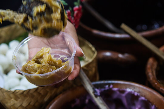 Action Shot of Vendor Scooping Brown Sweet Porridge with Ladle into Clear Cup