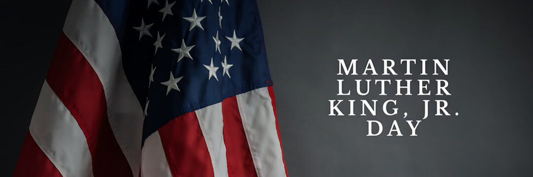 A close up of a folded american flag with white stars and red and white stripes next to the text martin luther king jr day on a dark background
