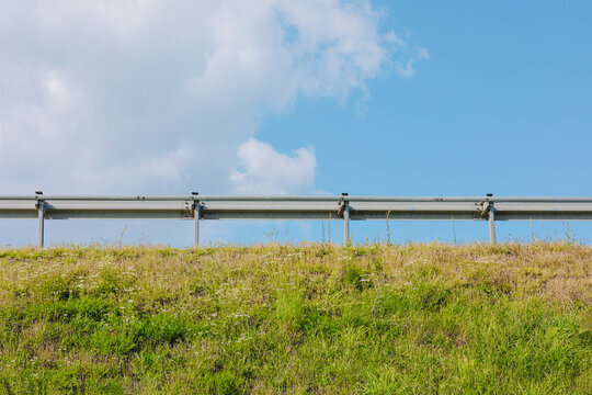 Metal Highway Guardrail on Grassy Roadside Embankment Under Blue Sky
