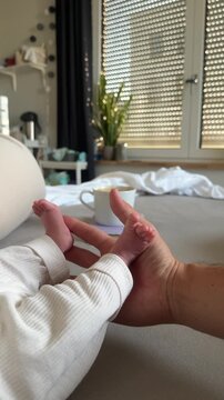 Tiny newborn baby feet cradled gently in a parent's hand beside a warm cup of coffee, capturing tender new parenthood, love and cozy family morning moments