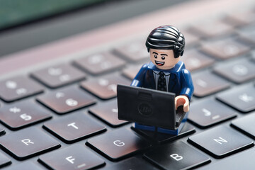 Fototapeta premium Tambov, Russian Federation - August 29, 2026 A happy Lego businessman minifigure sitting on a computer keyboard while working on a laptop.