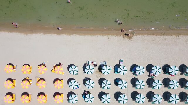 Top-down aerial drone view flying over rows of colorful beach umbrellas on sandy seashore in Cesenatico, Riviera Romagnola, Emilia-Romagna, Italy