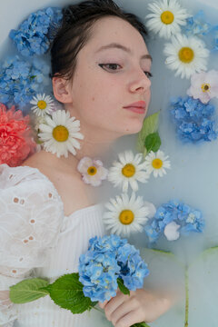 Young woman relaxing in floral milk bath with closed eyes and serene expression, with woman, young, portrait, relaxation detail, showing spa, milk, bath, milkbath context