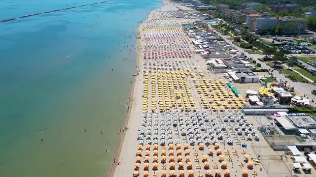 Top-down aerial drone view flying over rows of colorful beach umbrellas on sandy seashore in Cesenatico, Riviera Romagnola, Emilia-Romagna, Italy