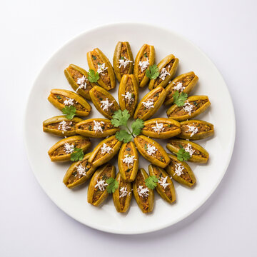 Traditional Potoler Dorma (stuffed pointed gourd) arranged geometrically on a white porcelain dish, white background
