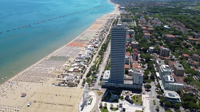 Aerial view of Cesenatico skyscraper and sandy beach lined with colorful umbrellas in Riviera Romagnola, Adriatic Sea, Emilia-Romagna, Italy
