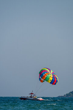 A motorboat tows a colorful rainbow parasail across the open sea under a clear blue sky.