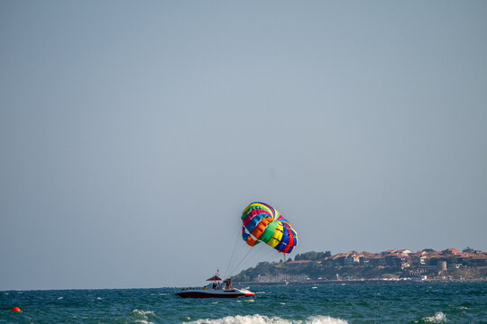 A motorboat tows a colorful rainbow parasail across the open sea under a clear blue sky.