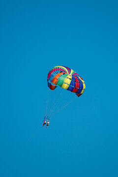 A colorful parasail carrying two people soars high in the clear blue sky.