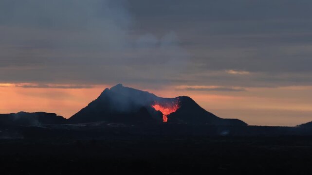 Fagradalsfjall volcano in Iceland erupting with glowing red lava flowing from the crater at beautiful orange sunset