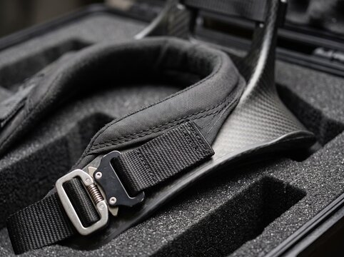 Carbon fiber camera neck support harness features durable metal buckles and padded fabric straps inside a protective black foam case