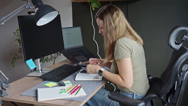 Woman places a sticky note in her notebook and writes at a home office desk.