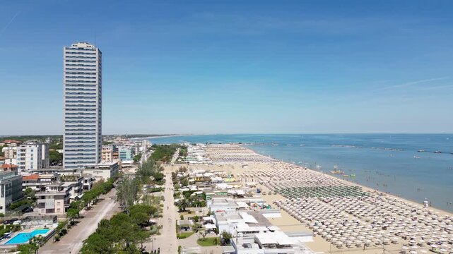 Aerial view of Cesenatico skyscraper and sandy beach lined with colorful umbrellas in Riviera Romagnola, Adriatic Sea, Emilia-Romagna, Italy