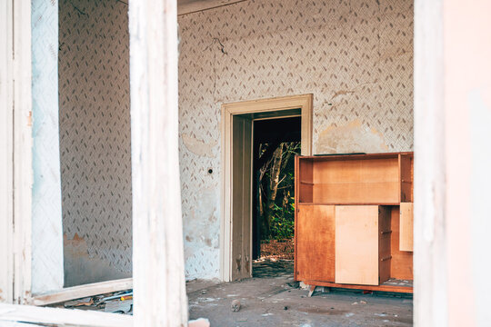 Old wooden sideboard inside a neglected room with damage and peeling wallpaper. Concept of urban decay, vintage home destruction, abandoned property, and passage of time.