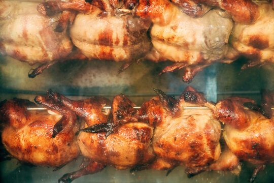 Whole chickens cooking in a commercial rotisserie spit grill with golden crispy skin. Concept of delicious street food, roasted poultry, catering service, and culinary preparation.