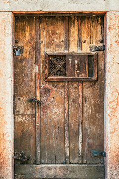 Rustic antique wooden door with iron hardware and a small viewing window. Concept of medieval architecture, security, historical preservation, secret entrances, and speakeasy hatches.