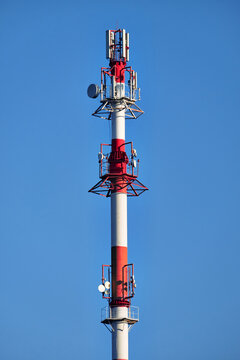 Red and white telecommunications tower with cellular antennas and communication equipment against a clear blue sky, isolated vertical composition with ample copy space