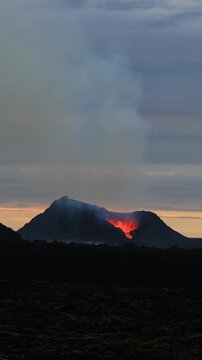 Fagradalsfjall volcano erupting with glowing lava, smoke, and ash in Iceland during a dramatic sunset