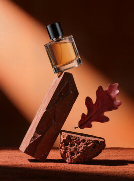 Amber glass bottle balanced on geometric red sandstone monolith with red autumn leaf and copy space, luxury perfume concept