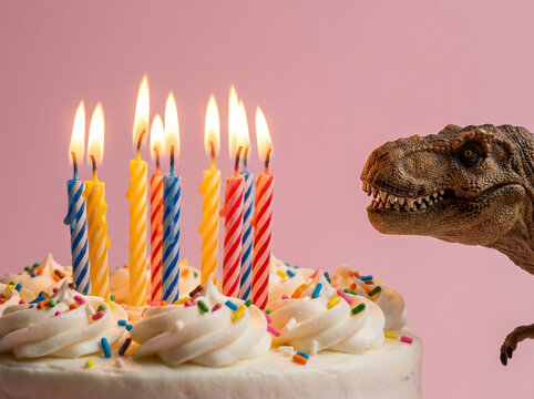 Lit birthday cake candles with toy dinosaur