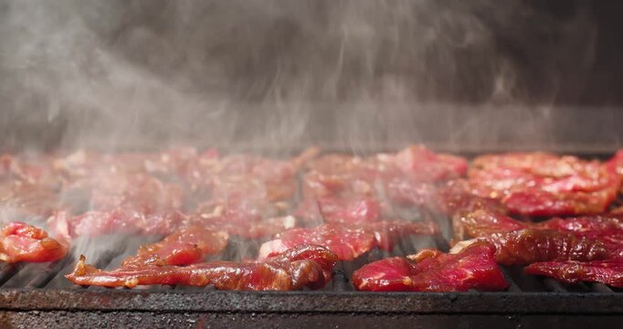 Slow pan right over red meat smoking in a pellet grill smoker to make delicious beef jerky. Smoke is rising over the grill. 